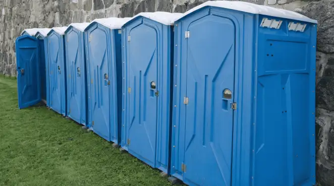 Row of blue portable toilets lined up on grass against a stone wall for event sanitation in Anaheim, CA