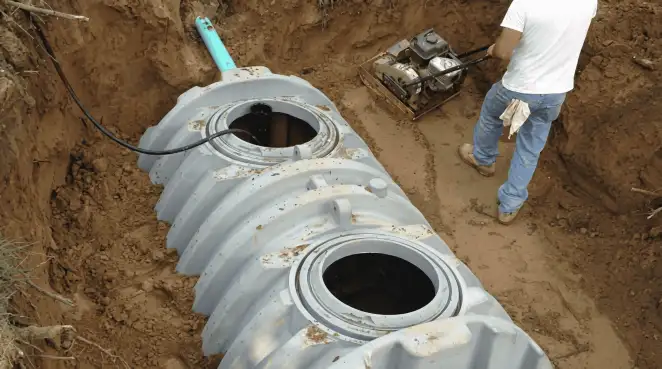 Septic tank installation showing a technician compacting soil around a new poly septic tank in an excavation pit in Anaheim, CA